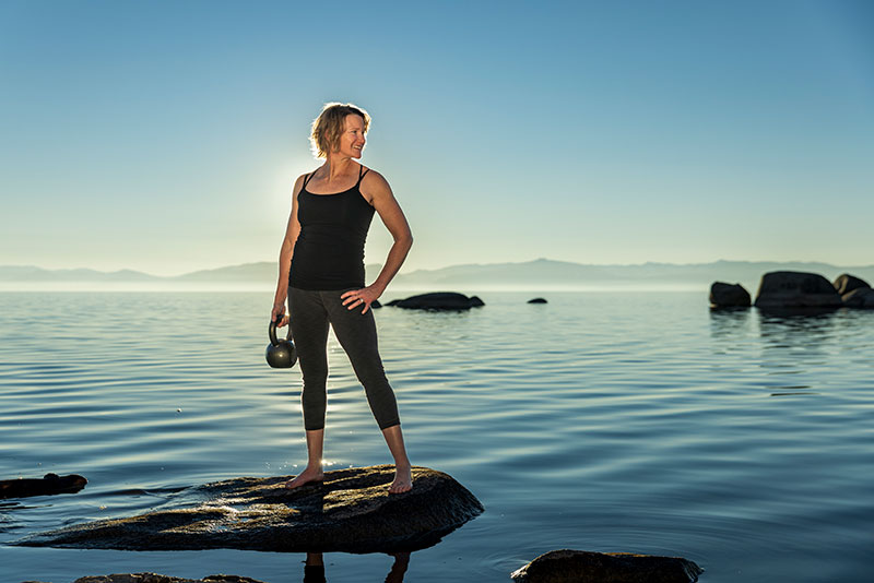 Trisha standing on a rock at Lake Tahoe with a kettlebell